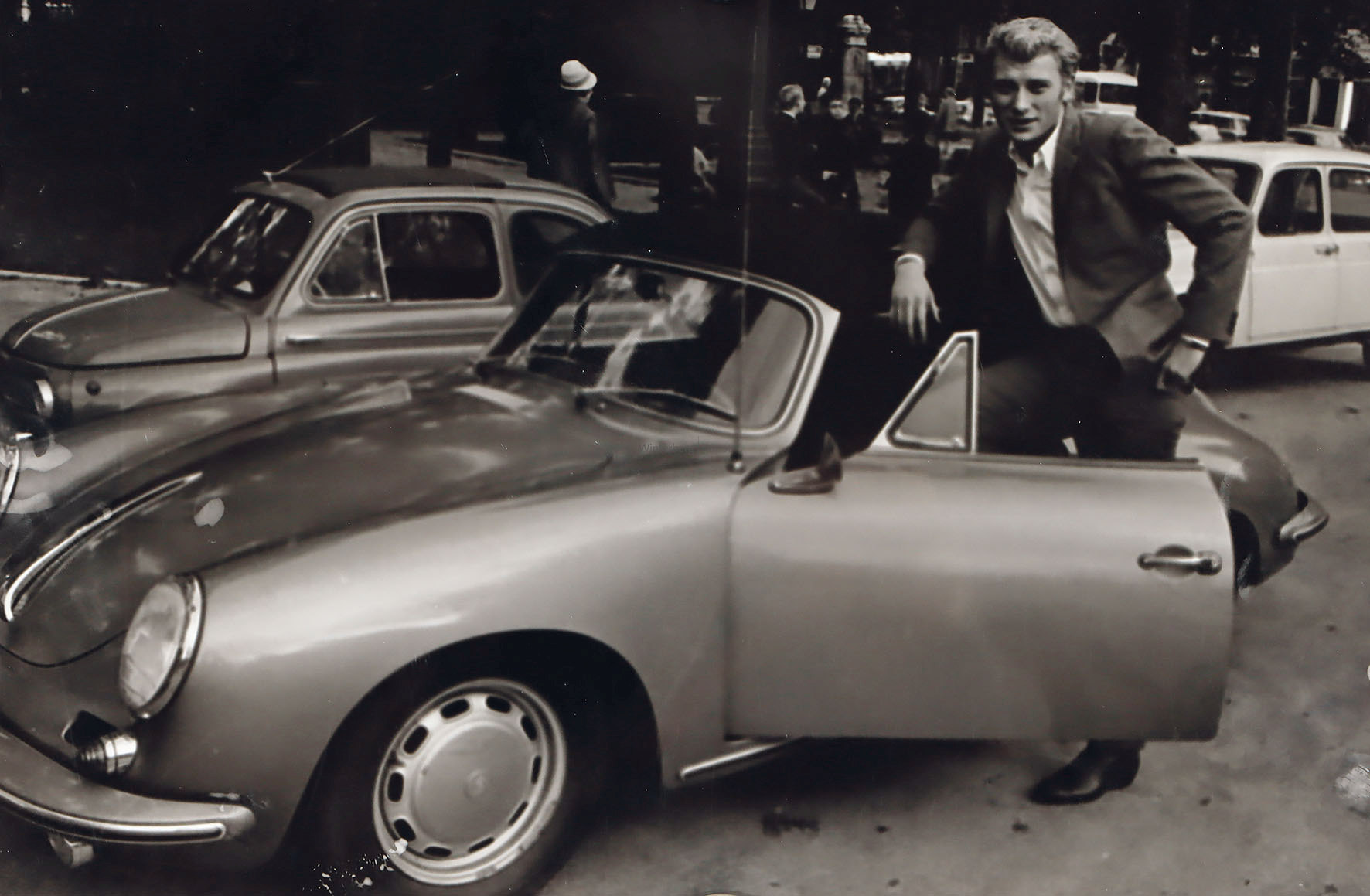 Der Sänger Johnny Halliday, bei einem Porsche Cabriolet stehend.